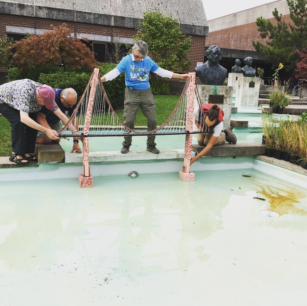 Four people building a miniature version of the famous Golden Gate Bridge in a fountain outside of Vallejo City Hall.